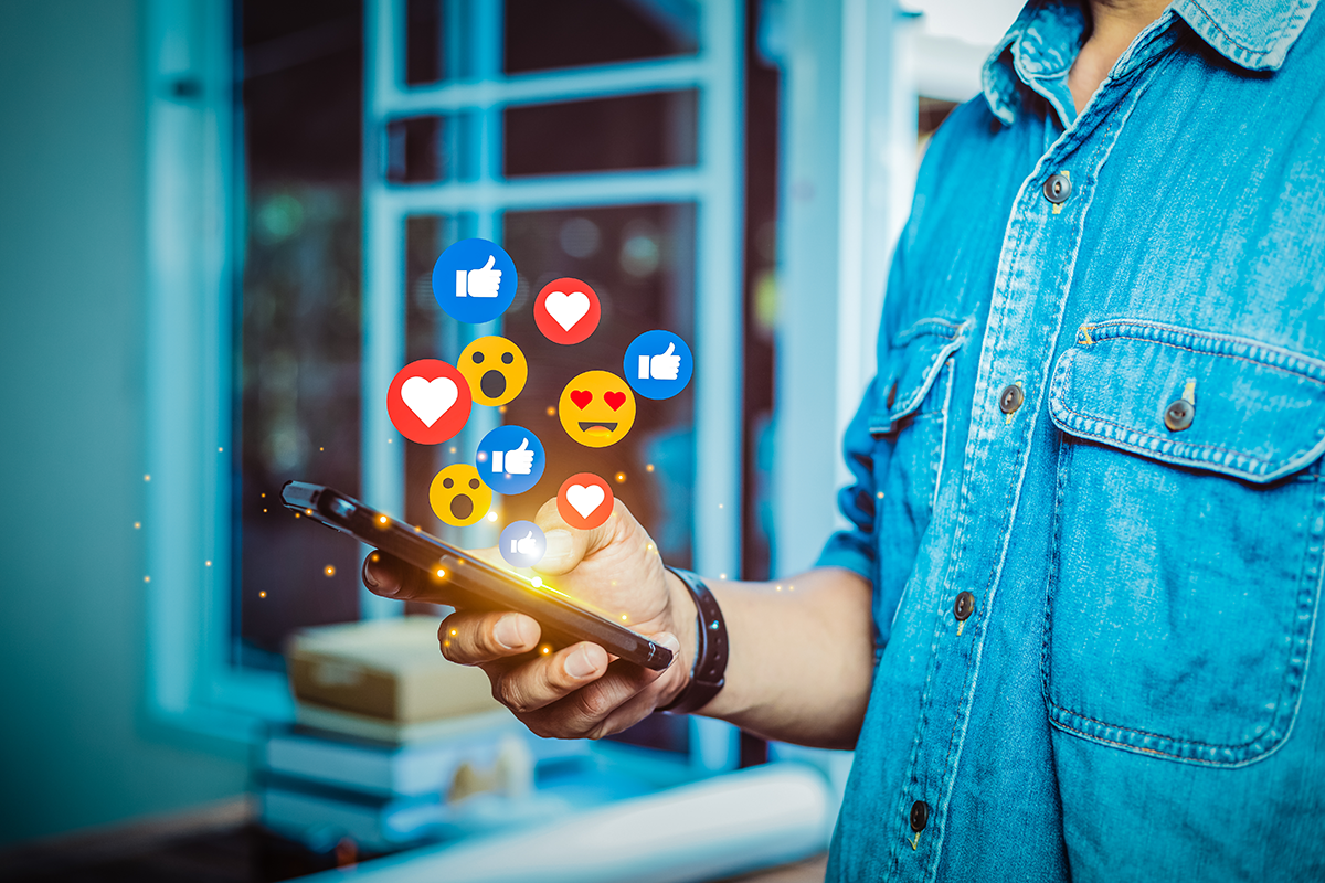 Man using smartphone to engage with social media, surrounded by floating reaction icons representing likes, hearts, and emotions, illustrating social media management and audience engagement strategies.