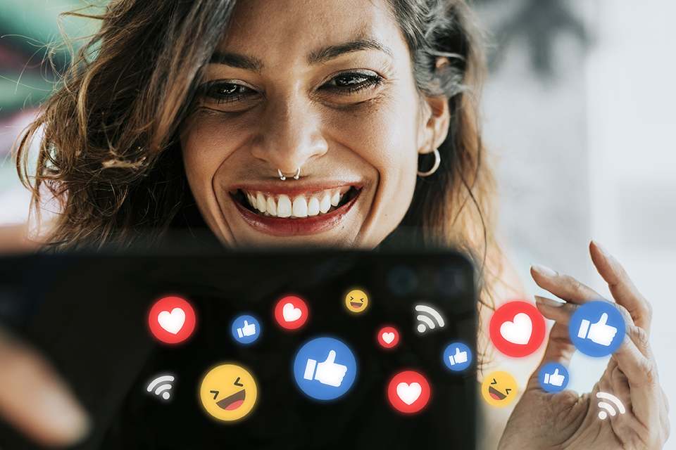Smiling woman interacting with smartphone surrounded by social media reaction icons, illustrating audience engagement and brand awareness in digital marketing.